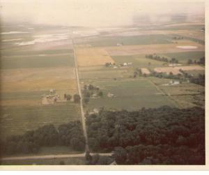 My house from the air, July 1970: My house is just to the right of the road in the center of the picture, surrounded by the little ring of trees. Note that our pond wasn't dug yet, and the farm across the road was still standing. (Don't die of nostalgia, anyone!)